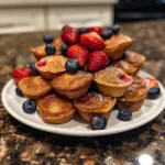 A close-up overhead shot of several mini pancake muffins with various mix-ins, including chocolate chips and berries.